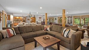 Un salon spacieux avec un grand canapé d’angle, une table basse en bois et un coin cuisine à l’arrière-plan.