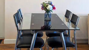 Une table à manger ornée d’un vase de fleurs, entourée de quatre chaises noires aux pieds chromés, dans une pièce au plancher en bois et aux murs blancs.