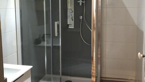 Una ducha a ras de suelo con puerta de cristal, panel de control y ducha de mano.