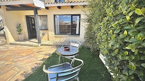 A patio with a table and chairs, a potted plant, and a building with a tiled roof and windows.