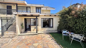 A two-story house with a stone patio, a small garden, and a dining area with outdoor furniture. - Ñireco House, discover Bariloche from Here. (San Carlos de Bariloche)