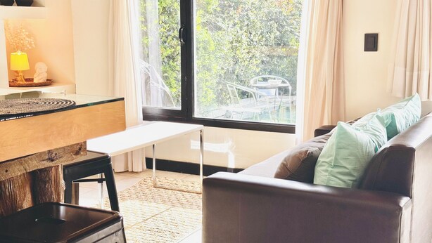 A modern living room with a sofa, a dining table, and a view of greenery outside. - Ñireco House, discover Bariloche from Here. (San Carlos de Bariloche)