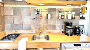 Een keuken met een roestvrijstalen spoelbak, een gasfornuis, een koffiezetapparaat en verschillende keukengerei op het aanrecht.
