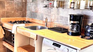A compact kitchen with a washing machine, a coffee maker, and a dish rack. - Ñireco House, discover Bariloche from Here. (San Carlos de Bariloche)