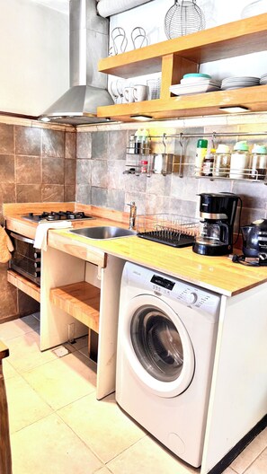 Een kleine keuken met een wasmachine, een koffiezetapparaat en een afwasschuurrek.