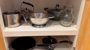 Una estantería en la cocina con distintos utensilios de cocina, incluyendo un hervidor, un colador, una olla y una jarra de vidrio.