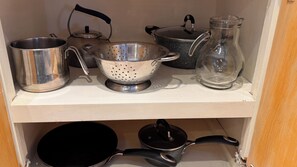 Une étagère de cuisine contenant divers ustensiles de cuisine, notamment une bouilloire, une passoire, une casserole et un pichet en verre.