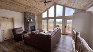 A spacious living room with a stone fireplace, leather furniture, large windows, and a wooden ceiling. - Brand New 4-bedroom cabin/stunning views/king bed, Hot Tub!!! (Jefferson)
