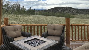 A covered outdoor seating area with a fire pit, wooden railings, and a view of a grassy field and mountains. - Brand New 4-bedroom cabin/stunning views/king bed, Hot Tub!!! (Jefferson)