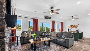 A spacious living room with a fireplace, two sofas, a coffee table, and a large window with red curtains. - Lakeview Home: Private Hot tub and Sauna (Branson)