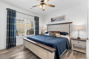 A bedroom with a bed, nightstands, a ceiling fan, a window with curtains, and a painting on the wall. - Lakeview Home: Private Hot tub and Sauna (Branson)
