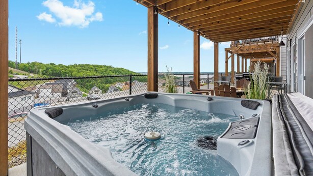 A hot tub with a wooden pergola overhead, a view of a green landscape, and outdoor furniture. - Lakeview Home: Private Hot tub and Sauna (Branson)