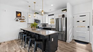 Une cuisine moderne dotée d’un îlot central, d’appareils électroménagers en acier inoxydable et de luminaires suspendus.