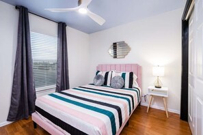 A bedroom with a bed, a ceiling fan, a bedside table with a lamp, and a window with curtains. - Art Deco 3 BR Near Fort Bliss (El Paso)