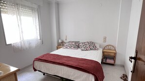 Ein Schlafzimmer mit einem Bett, einem Nachttisch, einem Fenster mit Vorhängen und einer Tür.