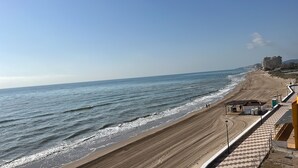 Ein Strand mit einem gepflasterten Gehweg, einer kleinen Struktur mit Sitzgelegenheiten und Blick auf den Ozean.