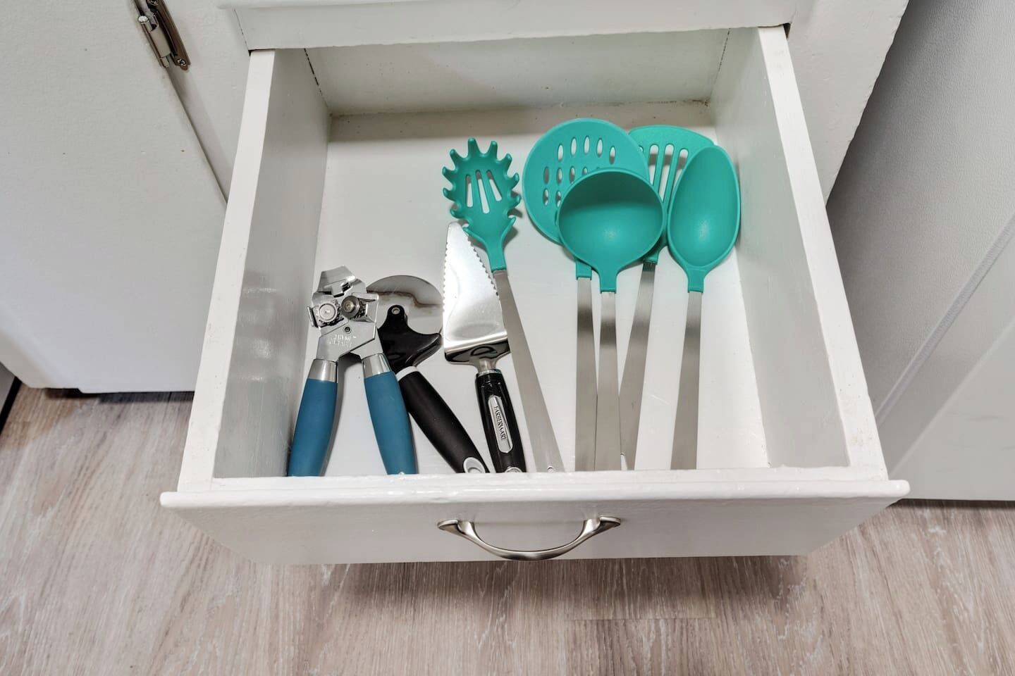 Un tiroir contenant divers ustensiles de cuisine, notamment une pince, une spatule et une paire de ciseaux.