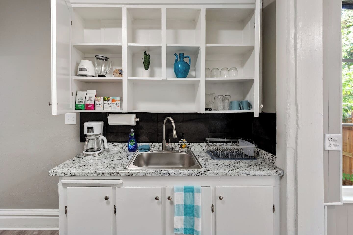 A kitchen with white cabinets, a granite countertop, a sink, a coffee maker, and a dish rack.