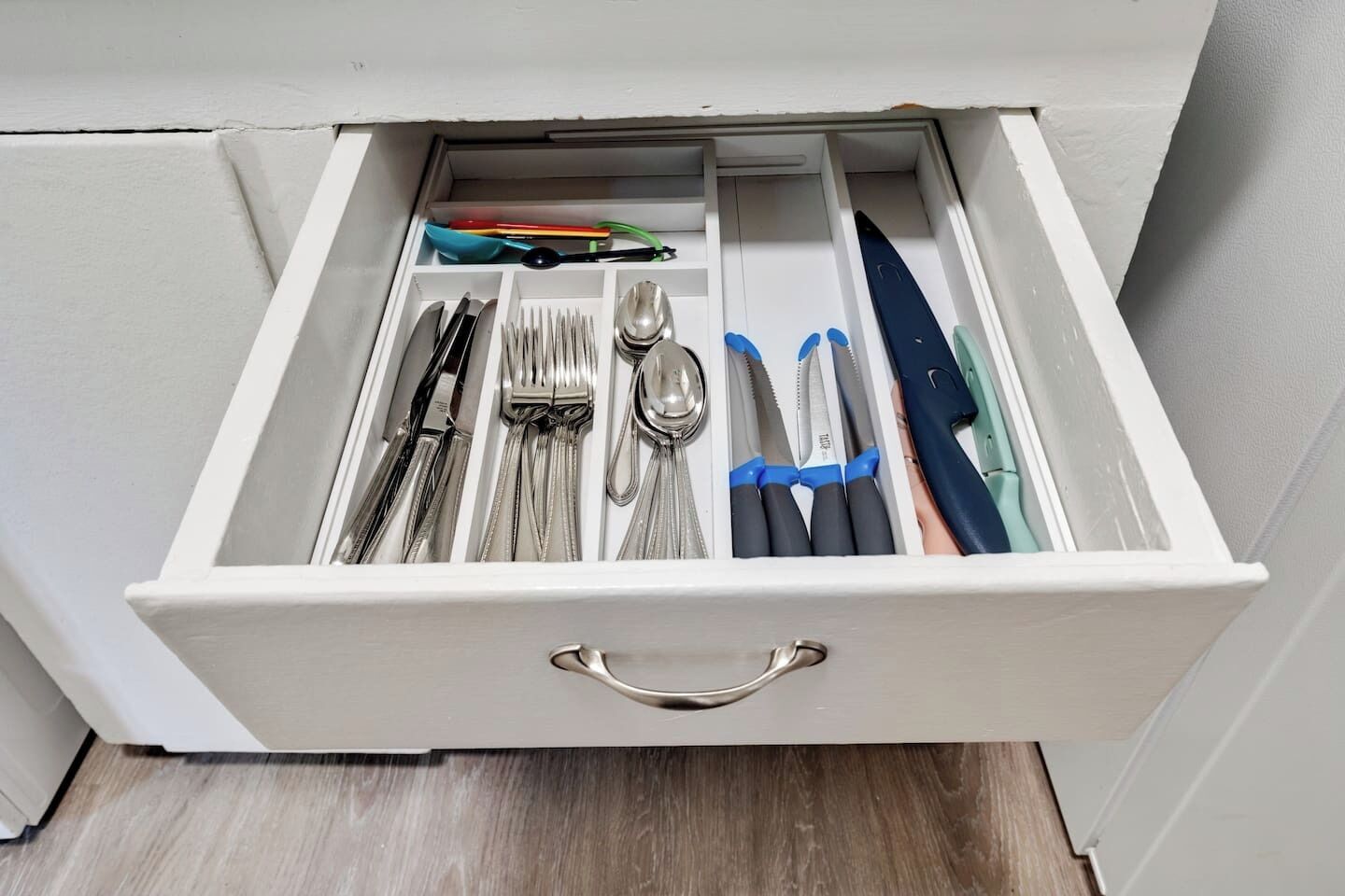 Uma gaveta com utensílios de cozinha bem organizados, incluindo garfos, facas e colheres.