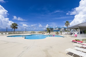 A pool area with lounge chairs, palm trees, and a building with blue roofs. - Refresh, Relax, and Recharge!  Family-sized Resort Beach condo. (Gulf Shores)