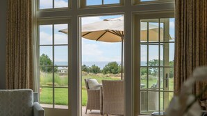 Una habitación con un amplio ventanal corredera que da a un patio exterior con mobiliario de mimbre y una gran sombrilla.