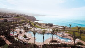 Un resort con varias piscinas, palmeras y vista al océano.