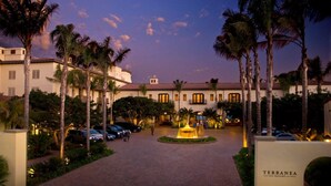 Entrada de hotel con una fuente, palmeras y un camino pavimentado.