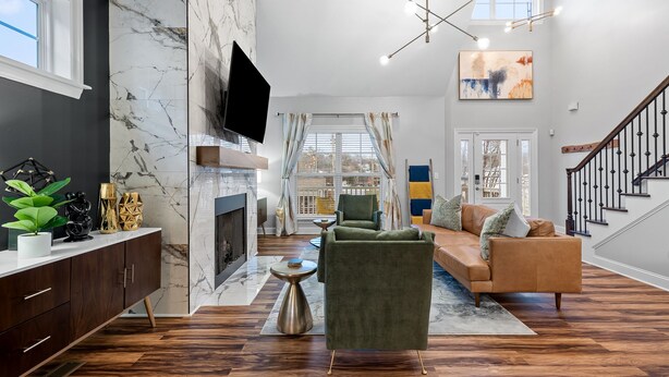 A modern living room with a fireplace, a green armchair, a sofa, and a staircase. - 3min to Aquarium | Secret Game Room | 3 King Beds (Chattanooga)