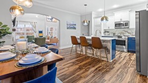 A modern kitchen with white cabinets, stainless steel appliances, and a wooden dining area with blue chairs. - 3min to Aquarium | Secret Game Room | 3 King Beds (Chattanooga)