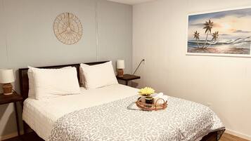 En snyggt bäddad säng med ett mönstrat överkast, två sänglampor, en dekorativ väggdekoration och en tavla som föreställer en strandscen.