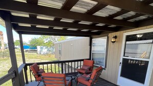 A covered outdoor seating area with a table and four chairs, a doormat with "hello" written on it, and a view of a house and trees in the background.