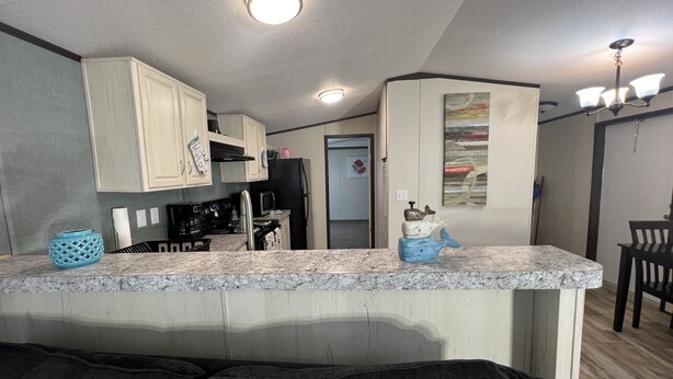 A kitchen with white cabinets, a black refrigerator, and a microwave. There is a blue decorative item on the counter.