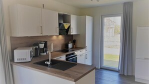 A modern kitchen with white cabinets, a wooden countertop, and a built-in oven. - Haus Nr. 37, Ferienhaus Deichgraf - Gepflegtes Ferienhaus, Sauna, Süd-terrasse, Loggia mit Meerblick (Wangerland)