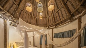Una habitación con cama, una silla, una hamaca y un techo de vigas trenzadas y luces colgantes.