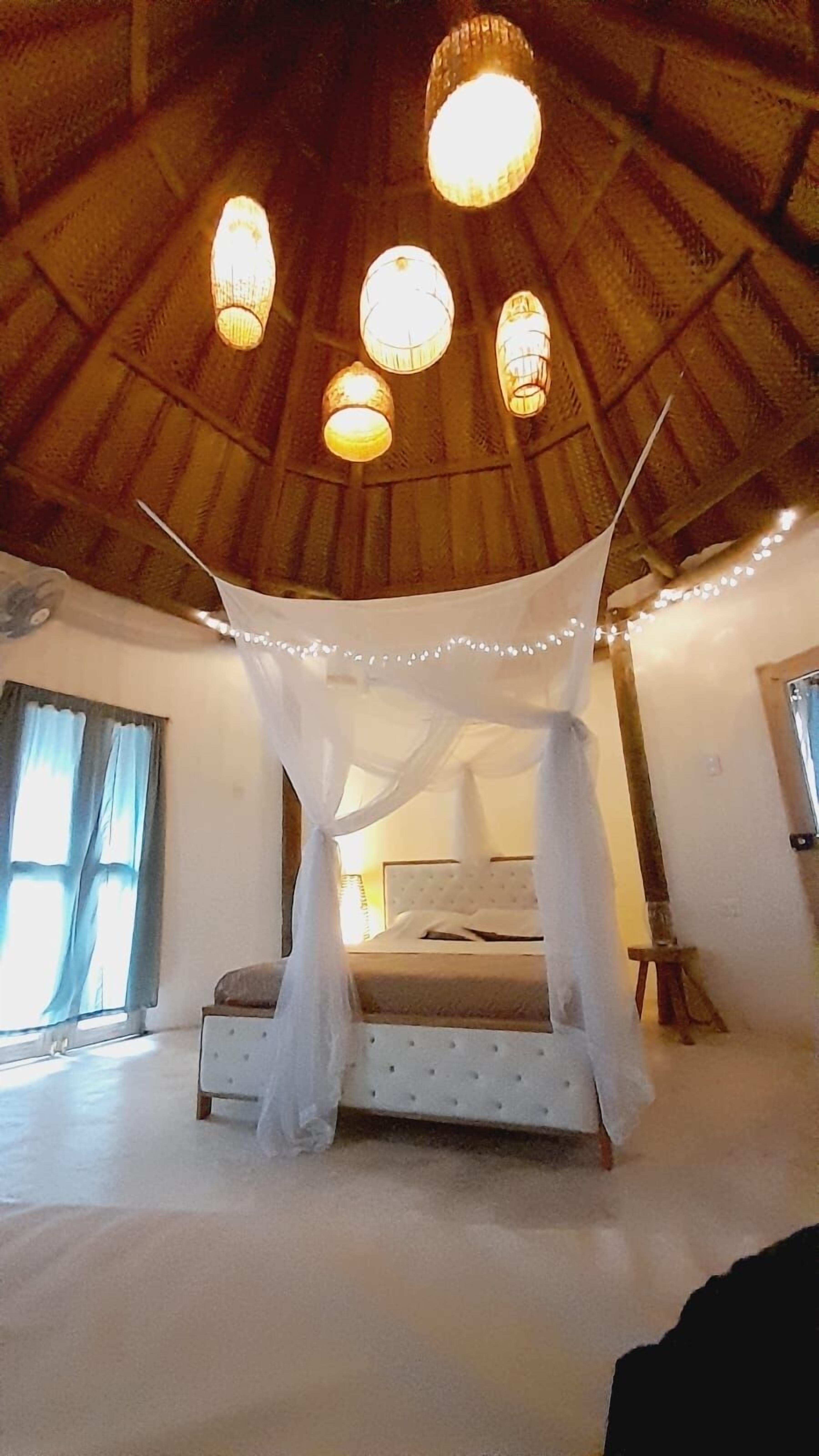 A bedroom with a bed under a canopy, a wooden ceiling, and a window with curtains.
