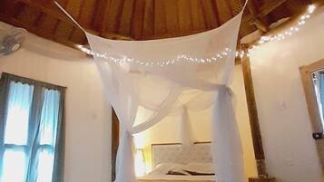 A bedroom with a bed under a canopy, a wooden ceiling, and a window with curtains.