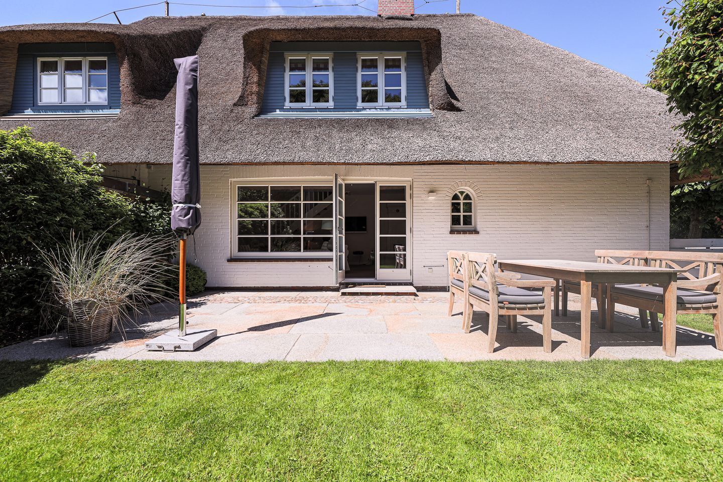 A house with a thatched roof, a patio with a table and chairs, and a covered outdoor area.