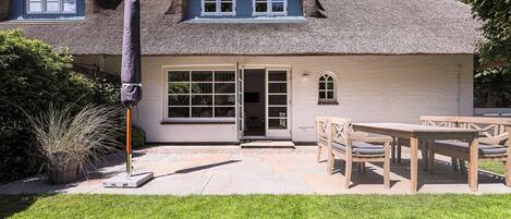 A house with a thatched roof, a patio with a table and chairs, and a covered outdoor area.