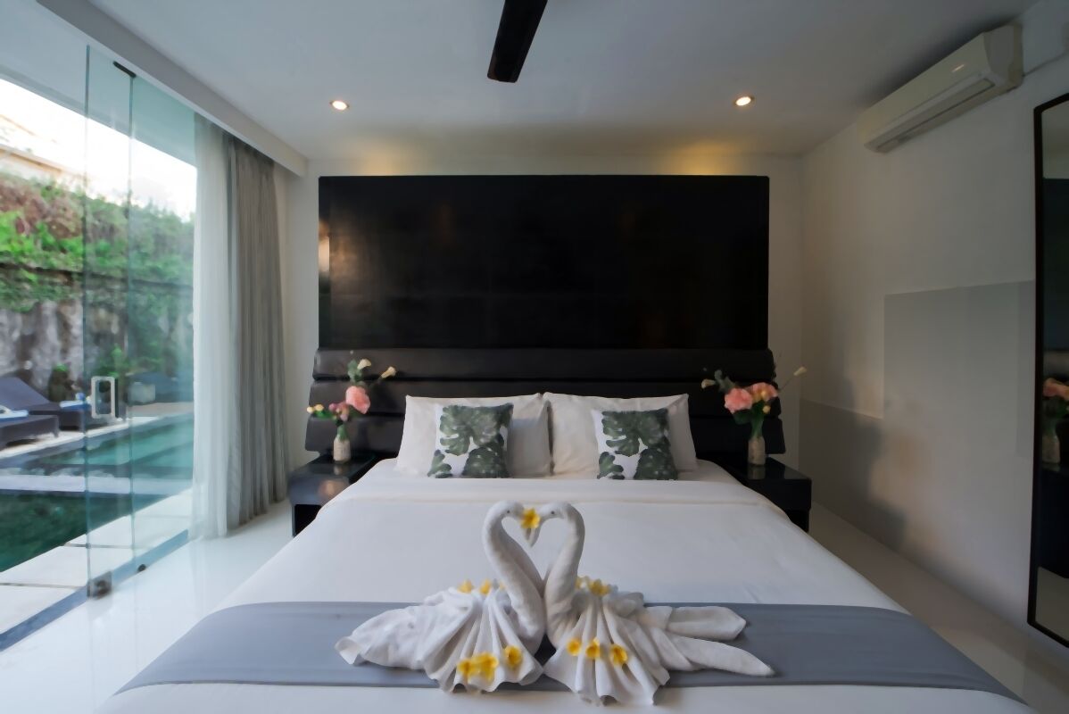 Una moderna camera d'albergo con un ampio letto, una televisione a schermo piatto, una parete vetrata e vista su un giardino.
