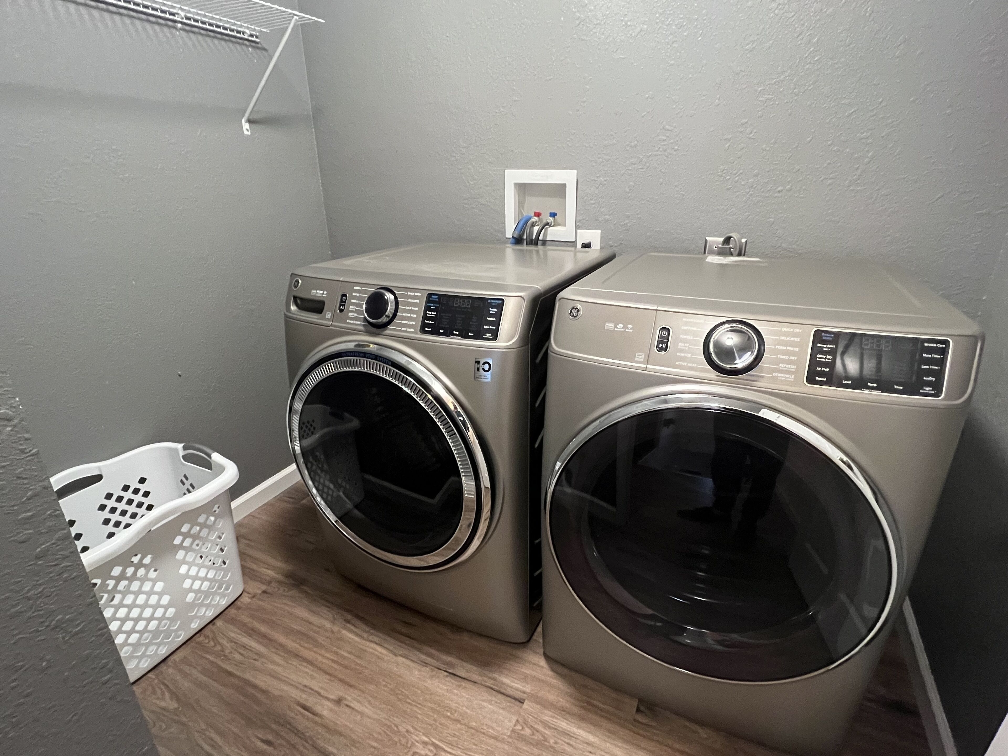 Two front-loading washing machines in a laundry area with a white basket and a small shelf with items.