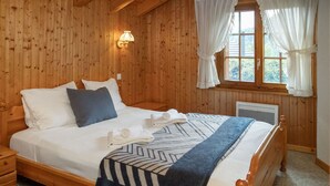 Ein Schlafzimmer mit Holzwänden, einem Bett, Kissen, einer Decke, einem Nachttisch, einer Wandleuchte und einem Fenster mit Vorhängen.