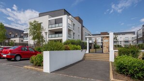 A modern apartment building with a gated entrance, a red car parked in the driveway, and a clear blue sky. - Cosy apartment for 4 guests with WIFI, TV and terrace (St-malo)