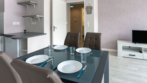 A dining area with a glass table set for four, two chairs, a TV on a white stand, and a door leading to another room. - Cosy apartment for 4 guests with WIFI, TV and terrace (St-malo)