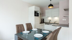 A modern dining area with a glass table, four brown chairs, and a kitchen in the background. - Cosy apartment for 4 guests with WIFI, TV and terrace (St-malo)