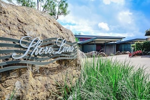 A sign with the text "Shore Limes" on a metal structure, set against a backdrop of a modern building and a rocky landscape. - Shorelines 01 - Hamilton Island (Whitsundays)