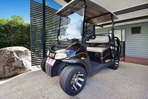 Carrinho de golfe estacionado em frente a uma casa com uma rocha grande e um portão de metal.