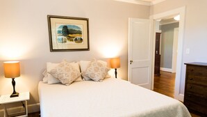 Une chambre à coucher avec un lit, deux lampes de chevet, un tableau encadré au mur et une commode en bois.
