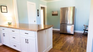Une cuisine avec des meubles blancs, un réfrigérateur en acier inoxydable et un plancher en bois.