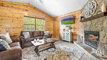 A cozy cabin interior with a fireplace, wooden walls, a leather sofa, and a television.