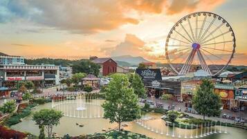 Um parque com uma grande roda-gigante, um lago com fontes e vários edifícios, incluindo um restaurante chamado 'Old Smoky'.